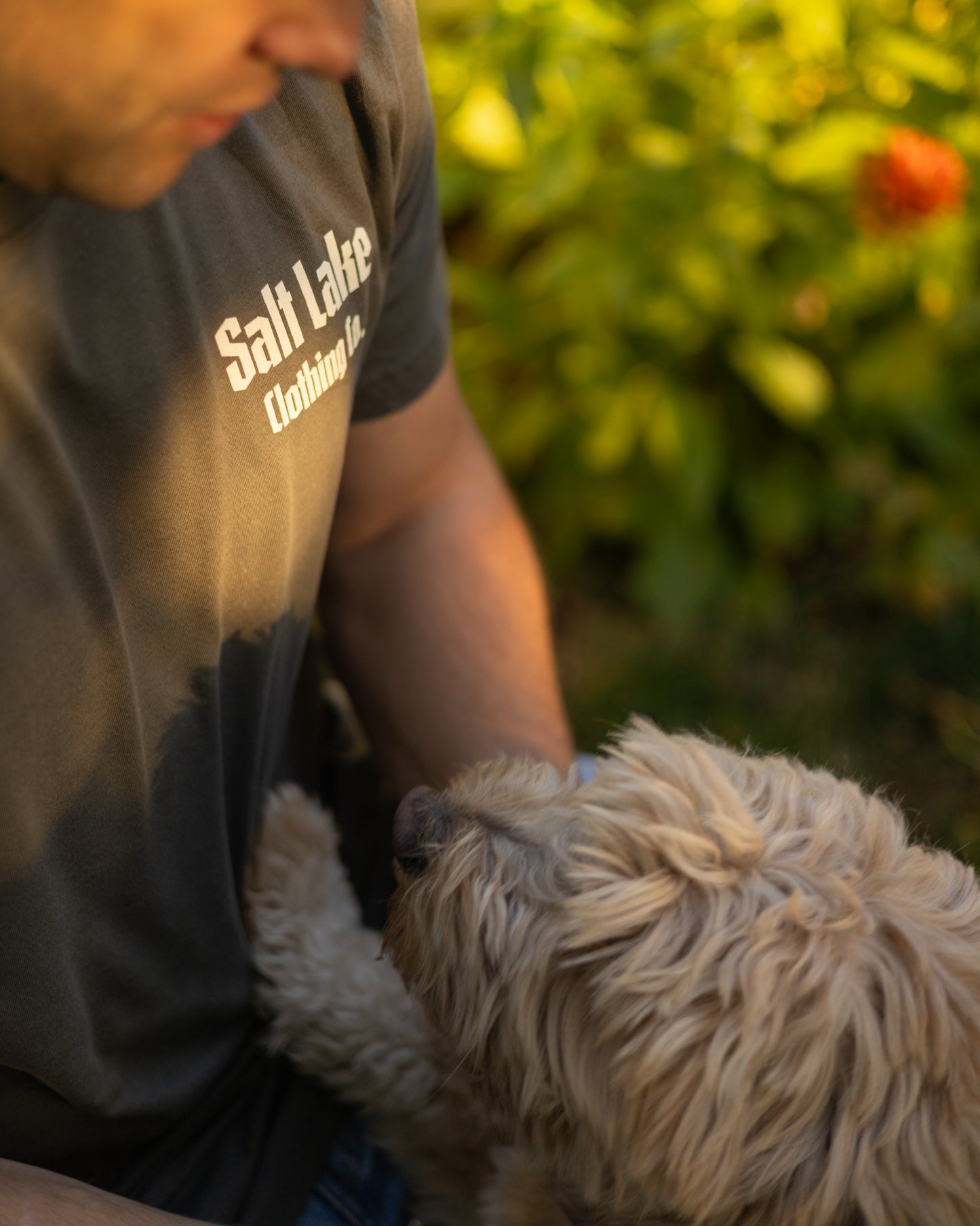 A man wearing the Good Company Pocket Logo T, petting a golden doodle dog in golden hour lighting.