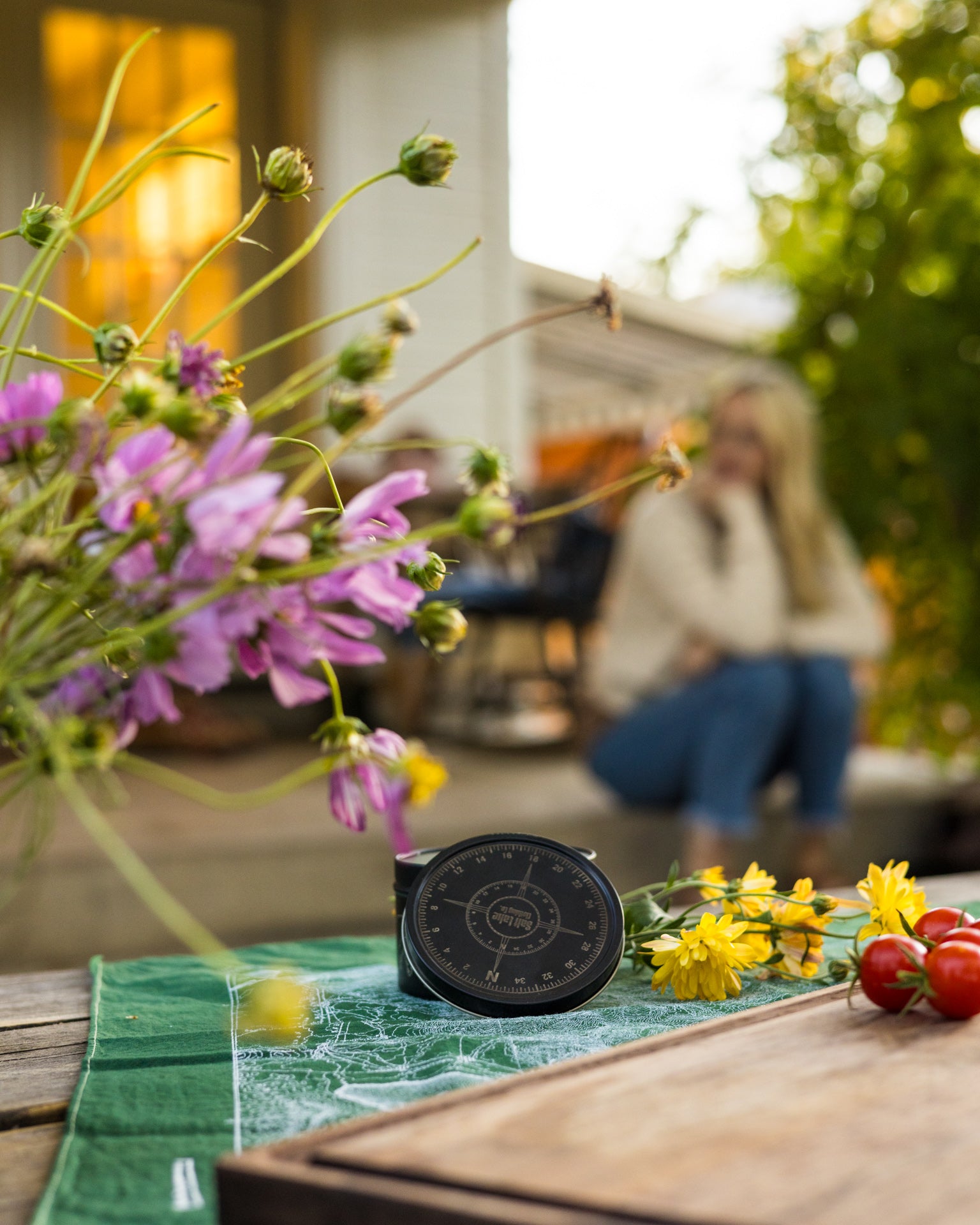 Olympus Pine Candle in etched metal tin with Wasatch Range design, displayed on a patio bench surrounded by flowers and vegetables.