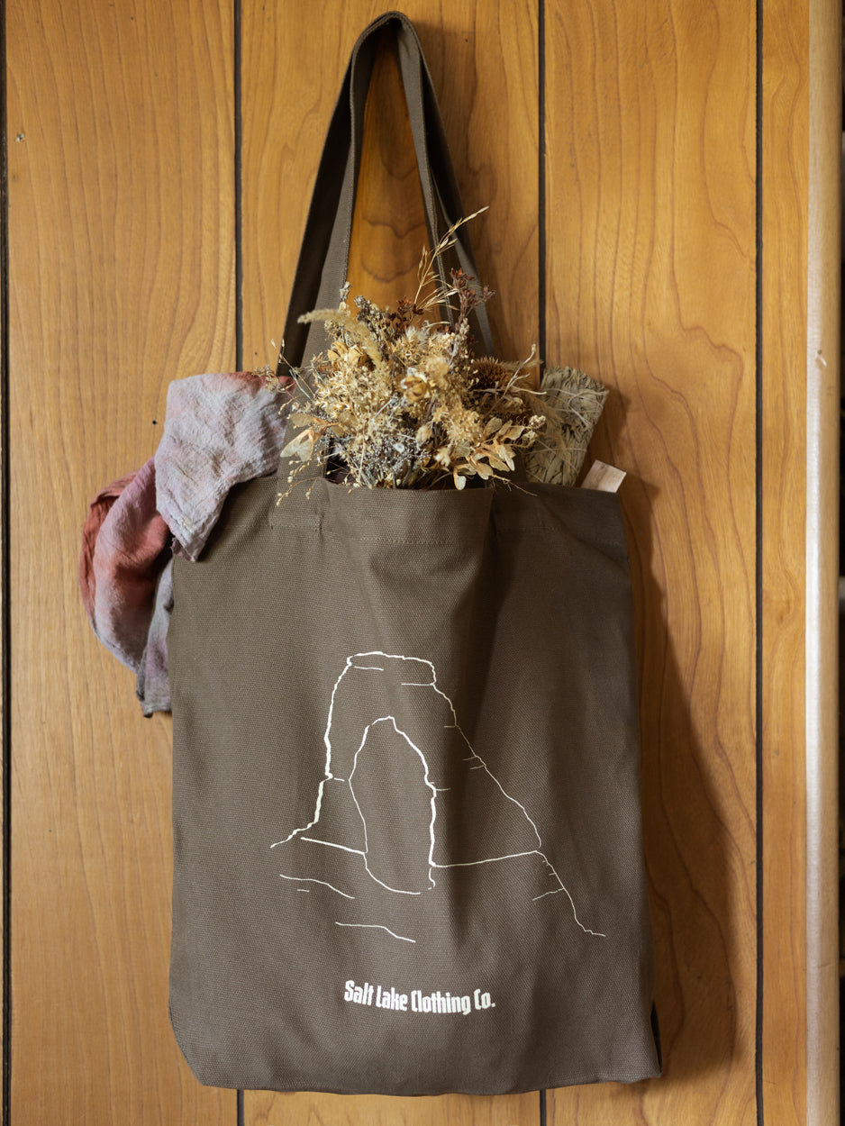 Close-up of Salt Lake Clothing Desert Tote - it is hanging against a vintage wooden wall, and is carrying dried flowers, and hand dyed fabrics.
