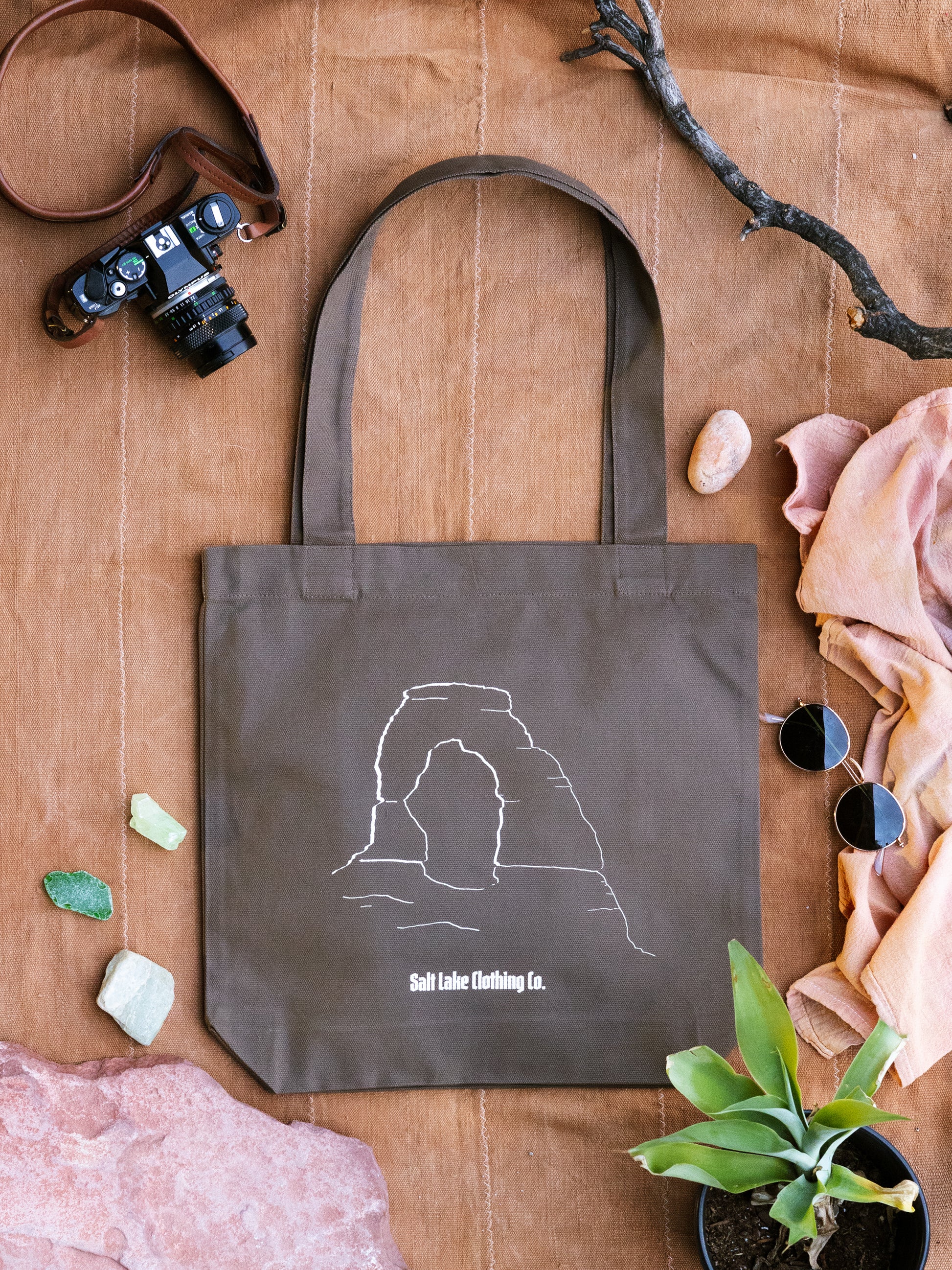 Close-up of Salt Lake Clothing Desert Tote surrounded by stones, gems, camera, sunglasses, and earth toned fabrics.